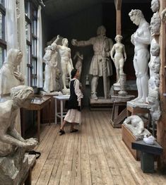 a woman looking at statues in a room with wooden floors and walls, along with windows