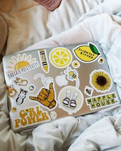 an open laptop computer sitting on top of a bed covered in white sheets and stickers