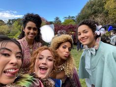 four women are posing for a photo in front of some trees and people wearing costumes