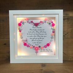 a heart shaped frame with pink flowers and hearts on it, in front of a wooden wall