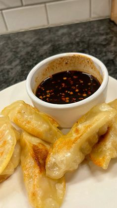 a white plate topped with dumplings next to a bowl of dipping sauce