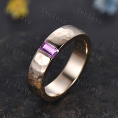 a gold ring with a purple stone in the center on a black table next to flowers