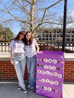 two young women standing next to a purple sign