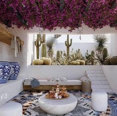 a living room filled with lots of white furniture and purple flowers hanging from the ceiling