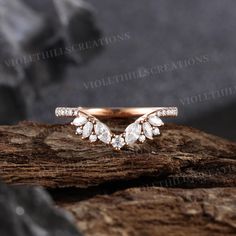 a rose gold wedding ring with three pear shaped diamonds on top of a piece of wood