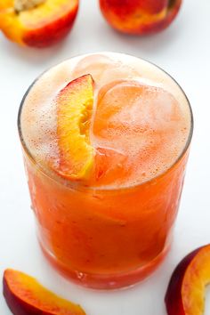 a glass filled with ice and fruit on top of a white table next to sliced peaches