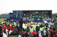 a group of people sitting on top of a lush green field next to a truck