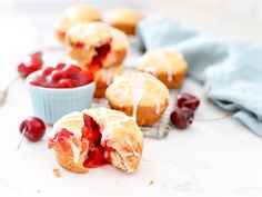 cherry muffins with icing and fresh cherries on a white counter top