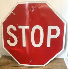 a red stop sign sitting on top of a wooden floor next to a white wall