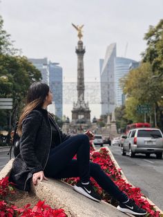 a woman sitting on the edge of a wall with red flowers in front of her