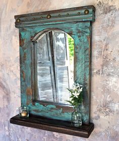 a mirror and vase with flowers on a shelf in front of a wall painted blue