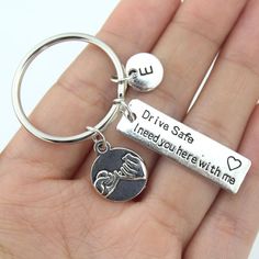 a hand holding a silver keychain that says drive safe, i need you here with me