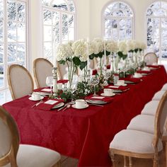 a long table is set with white flowers and place settings in front of large windows