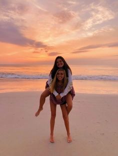 two women are playing on the beach at sunset with their arms around each other and smiling