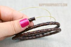 a woman's hand holding three brown and pink braided bracelets with gold rings