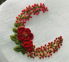 a close up of a piece of embroidery on a table cloth with red flowers and green leaves