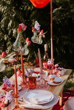 a table set with plates, glasses and candles for an outdoor dinner party in the woods