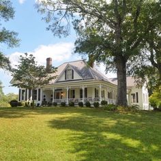 a large white house sitting in the middle of a lush green field next to trees