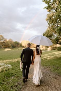 a bride and groom walking down a path under an umbrella with a rainbow in the background