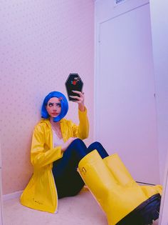 a woman with blue hair sitting on the floor holding up a cell phone in front of her face