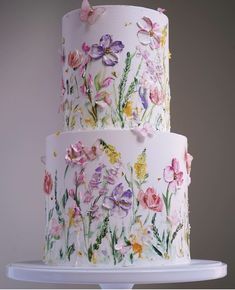 a three tiered cake decorated with flowers and butterflies on a white platter in front of a gray background