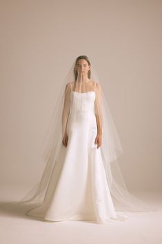 a woman in a white wedding dress with a veil on her head, standing against a beige background