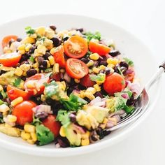 a white plate topped with a salad covered in corn and black beans next to a fork