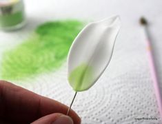 a hand holding a white flower on top of a piece of paper next to paint