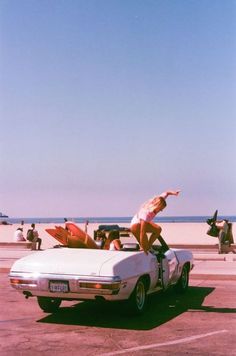 a man riding on the back of a white car in a parking lot next to the ocean