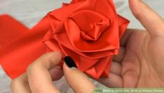 someone is making an origami rose out of red paper