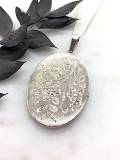 A Lovely Large Vintage Sterling Silver Oval Locket.  Beautifully hand engraved flowers on the front with a textured finish on the back.  It is stamped on the top bail SILVER.  The locket is in perfect working condition, it opens and closes perfectly and securely.  Inside the locket it has both original frames for your photos.  The locket measures 2.2 inches including the top bail.  It's on a new Sterling Silver 18 inch curb chain. Elegant Stamped Flower Pendant Necklaces, Elegant Stamped Flower Pendant Necklace, Heirloom Flower Engraved Jewelry, Heirloom Flower-shaped Engraved Jewelry, Antique Engraved Flower Jewelry, Antique Flower Engraved Jewelry, Silver Oval Jewelry With Flower Charm, Elegant Memorial Jewelry With Flower Charm, Antique Engraved Locket Necklace With Flower Pendant