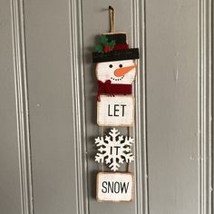 a snowman hanging on the front door with let it snow written in wood blocks