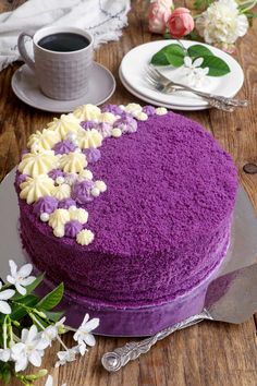 a purple cake sitting on top of a table next to a cup of coffee and saucer