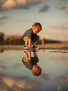 a little boy playing with his reflection in the water