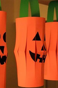 some paper bags with pumpkin faces on them hanging from the ceiling in front of a wall