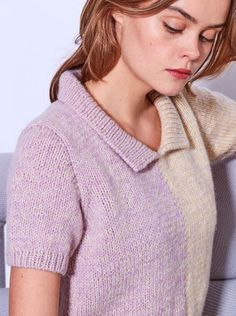 a woman sitting on a couch wearing a purple sweater and holding her head in her hands