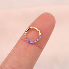 a person's finger with a small gold ring on top of their finger and blue opal stones in the middle