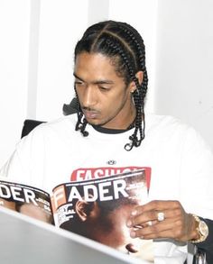 a man with dreadlocks reading a magazine while sitting at a desk in front of a computer