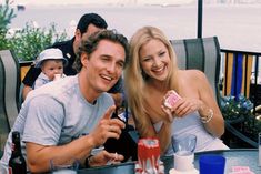 a man and woman sitting at a table with drinks in front of them, posing for the camera