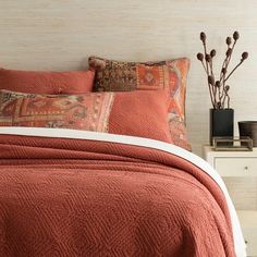 a bed with an orange bedspread and pillows on top of it next to a night stand