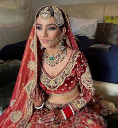 a woman in a red and gold bridal outfit sitting on a bed wearing jewelry