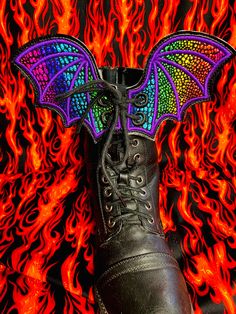 a pair of black boots with colorful wings on them sitting in front of a fire background