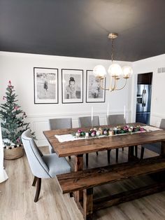 a dining room table with two benches and pictures on the wall above it, in front of a christmas tree