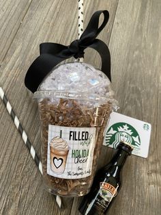 a starbucks cup filled with coffee beans and topped with a black ribbon, next to a bottle of beer