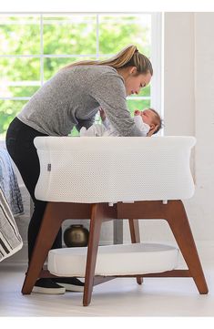 a woman holding a baby in her arms while standing next to a foot stool with a mattress on it