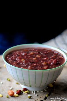 a white bowl filled with red beans on top of a wooden table next to a spoon