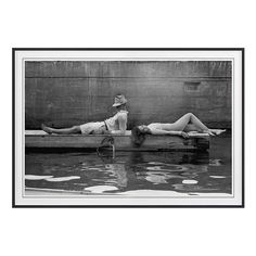 two women laying on the edge of a body of water