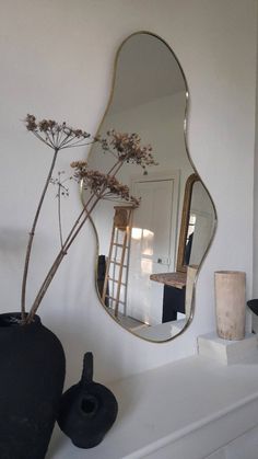 a mirror sitting on top of a white mantle next to a vase with flowers in it