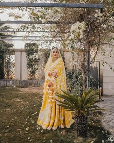 a woman wearing a yellow and white dress standing in front of a tree with flowers