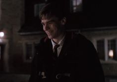 a smiling young man in a coat and tie standing outside at night with street lights behind him